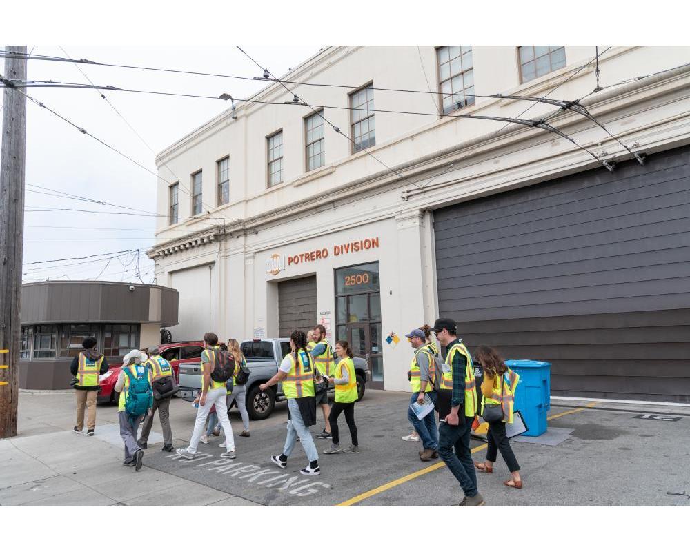 Several people wearing yellow safety vests begin a tour outside the Potrero Yard. Several people wearing yellow safety vests begin a tour outside the Potrero Yard.