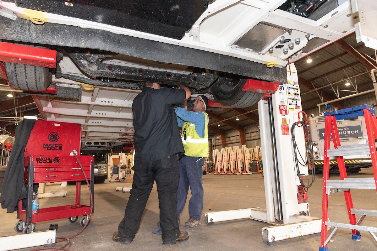 Workers underneath a bus making repairs.