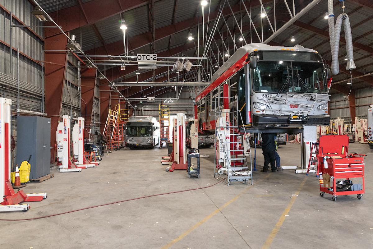 Bus on a lift with workers underneath making repairs. 