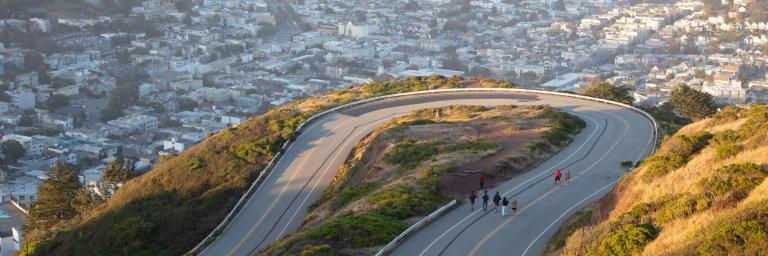 People walking up to Twin Peaks with the city skyline in the background