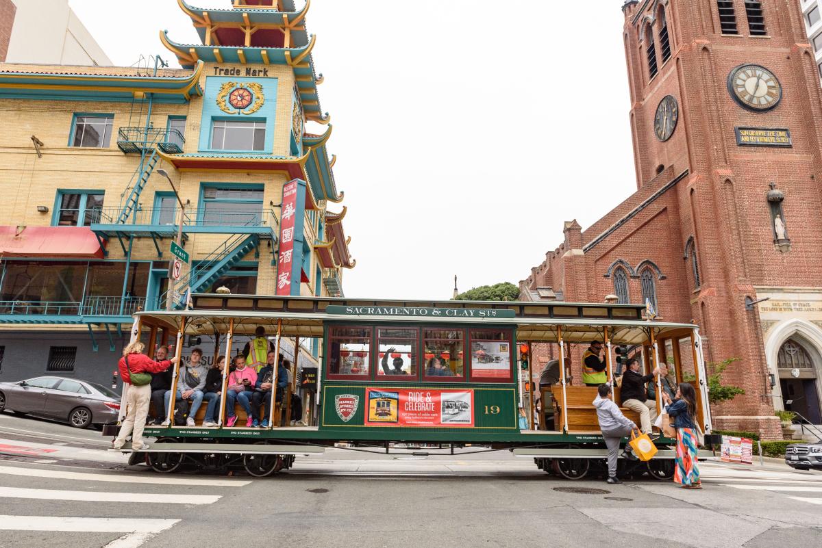 Cable car with a sign that says "Sacramento & Clay St" stops in Chinatown near a red brick church. Cable car with a sign that says "Sacramento & Clay St" stops in Chinatown near a red brick church.
