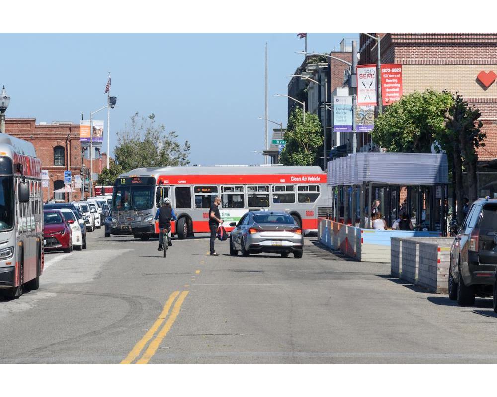 19 Polk Bus turning onto Beach Street while a biker bikes and passenger loading occurs in front of Ghirardelli Square