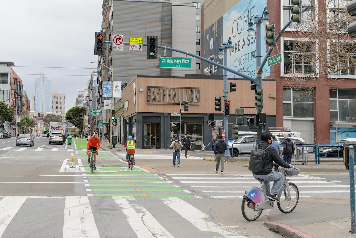 People use a two-way bikeway as others cross an intersection.
