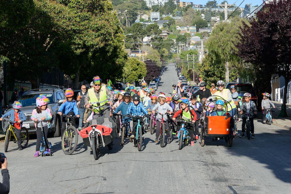 Many young people and adults ride bicycles down a residential street.
